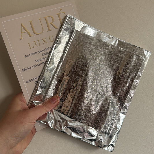 Hand holding a silver foil packet with 'Aure' branding in the background.
