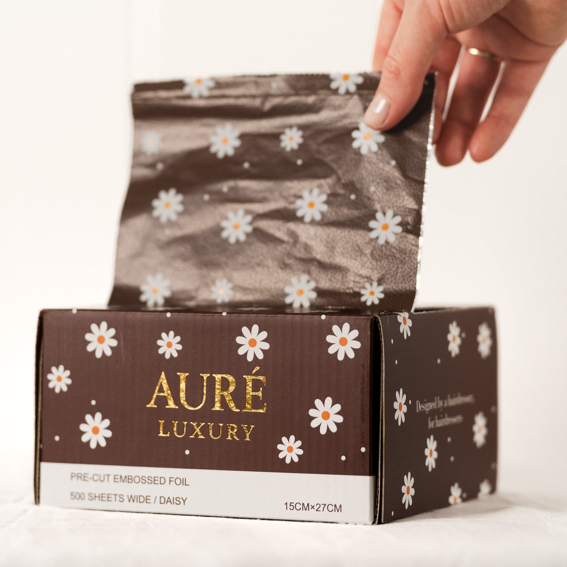 Hand opening a box of Aure Luxury tissue paper with floral design on a white background